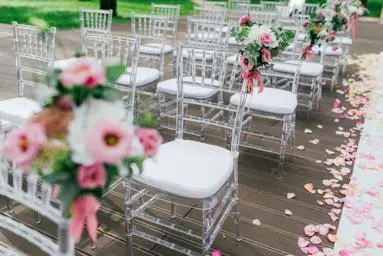 white plexi chairs lined up to create wedding aisle, pink, white and green flower decorations attached