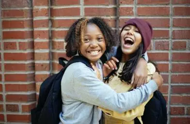 Two young people hugging in front of a brick wall