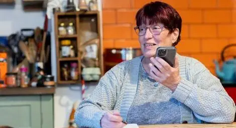 Woman using a phone on loudspeaker with a pen in her hand.
