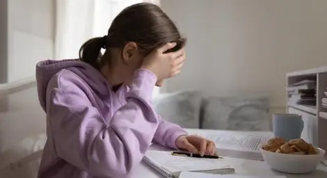 Young school girl holding head and writing in journal, feeling anxious and sad