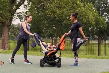 Two mums with prams stretching in a park getting ready to run