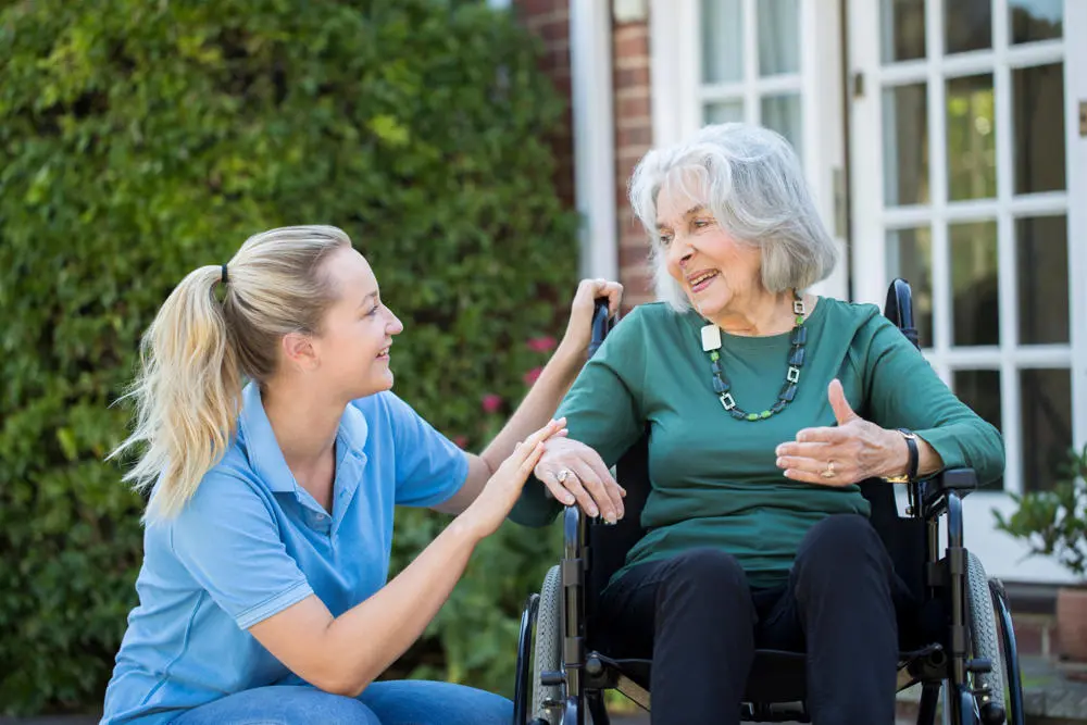 Older lady in a wheelchair chatting to a carer who is knelt down next to her.
