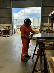 man using an angle grinder on sheet metal dressed in safety clothing 