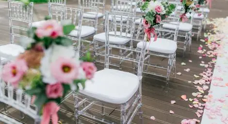 white plexi chairs lined up to create wedding aisle, pink, white and green flower decorations attached