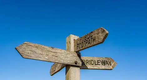 A wooden footpath sign stands in front of a clear blue sky