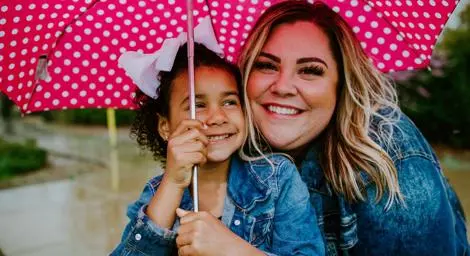 Foster mother and daughter smiling and holding a pink polka dot umbrella