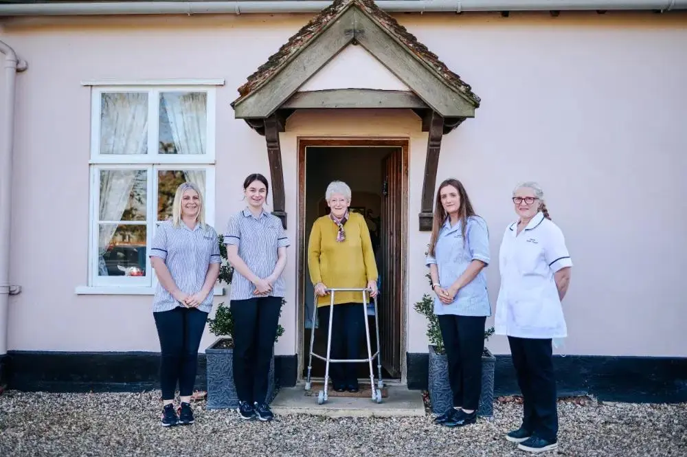 A group of carers in front of an older persons house who is standing in the middle of the photo.