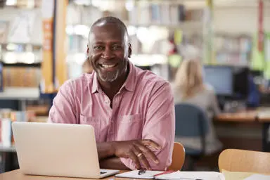 Man sitting with laptop in a library and smiling