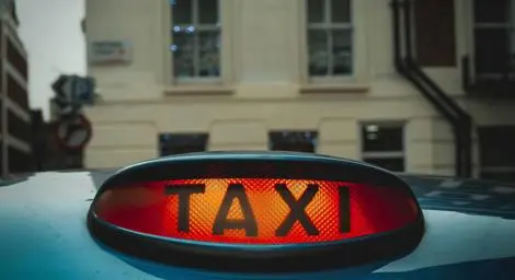 A lit up taxi sign sitting on the roof of a vehicle.