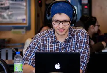 Man wearing check shirt sitting with headphones working on laptop in cafe