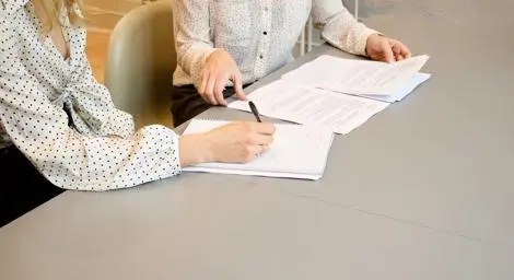 Two women in an office working together on a project, writing in a notepad