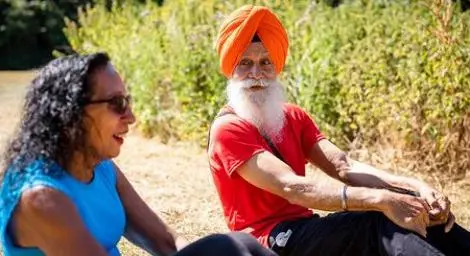 Old Sikh man exercising and doing sit ups with a woman in a park on a sunny day