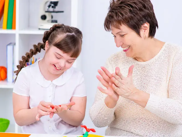 A teacher and young girl are molding play-doh together, they are both happy and smiling.