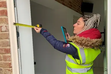 Sophia Gentile wearing a high vis jacket and measuring a door with a tap measure