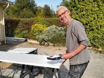 Steve Huxley painting wood with white paint outside in a garden