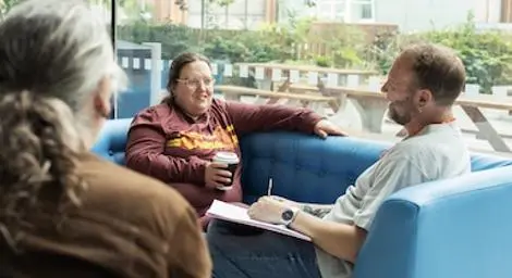 Three people having a drink in a cafe. Two are facing the camera. One is facing away.