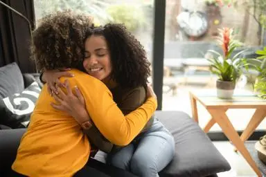 Mother and teenager hugging and smiling sitting on the sofa