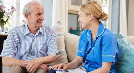 Older man sitting on a sofa with his carer going through paperwork