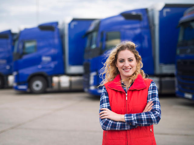 Woman in red jacket standing in front of blue lorries