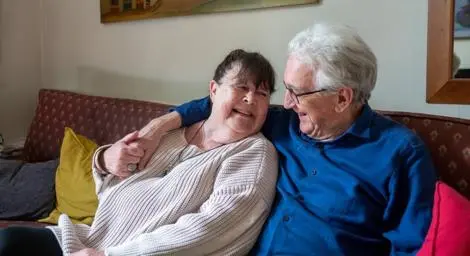 Man and woman couple sitting on a sofa holding hands hugging and smiling at each other